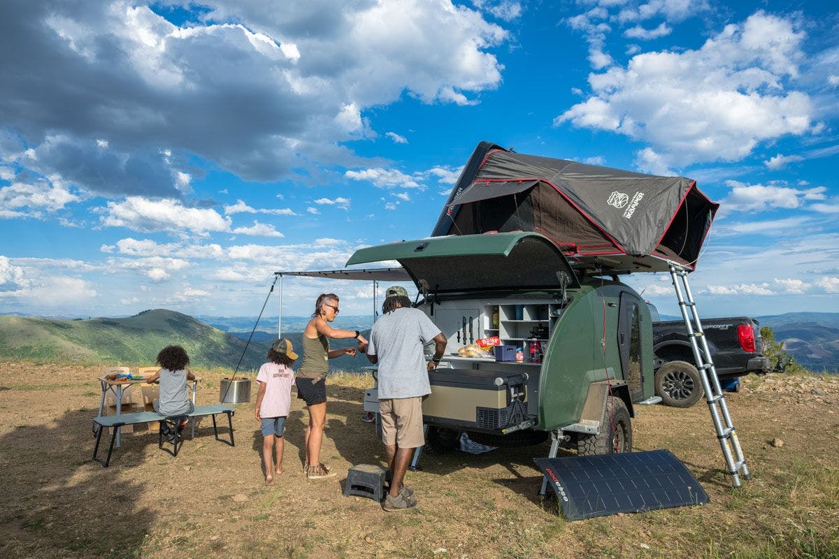 A photo with a family cooking in their TOPO2, a premium adventure trailer.