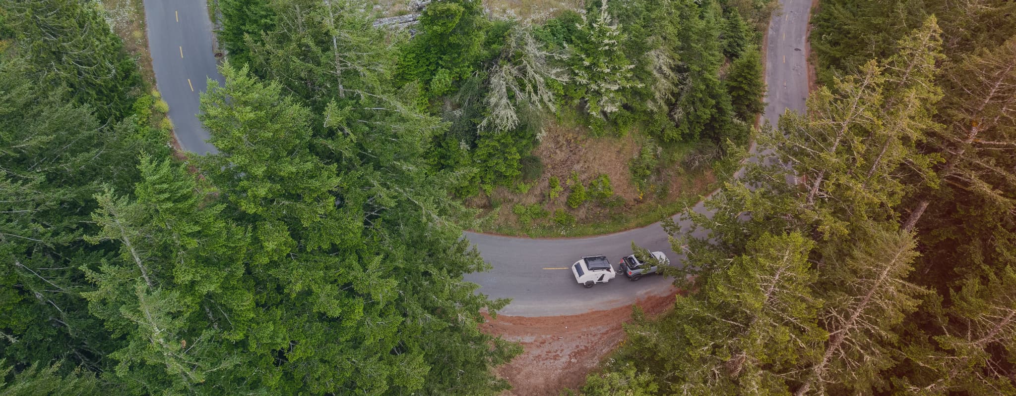 A winding forest road seen from above, with an Escapod TOPO2 trailer being towed through lush greenery, showcasing its off-road capability.