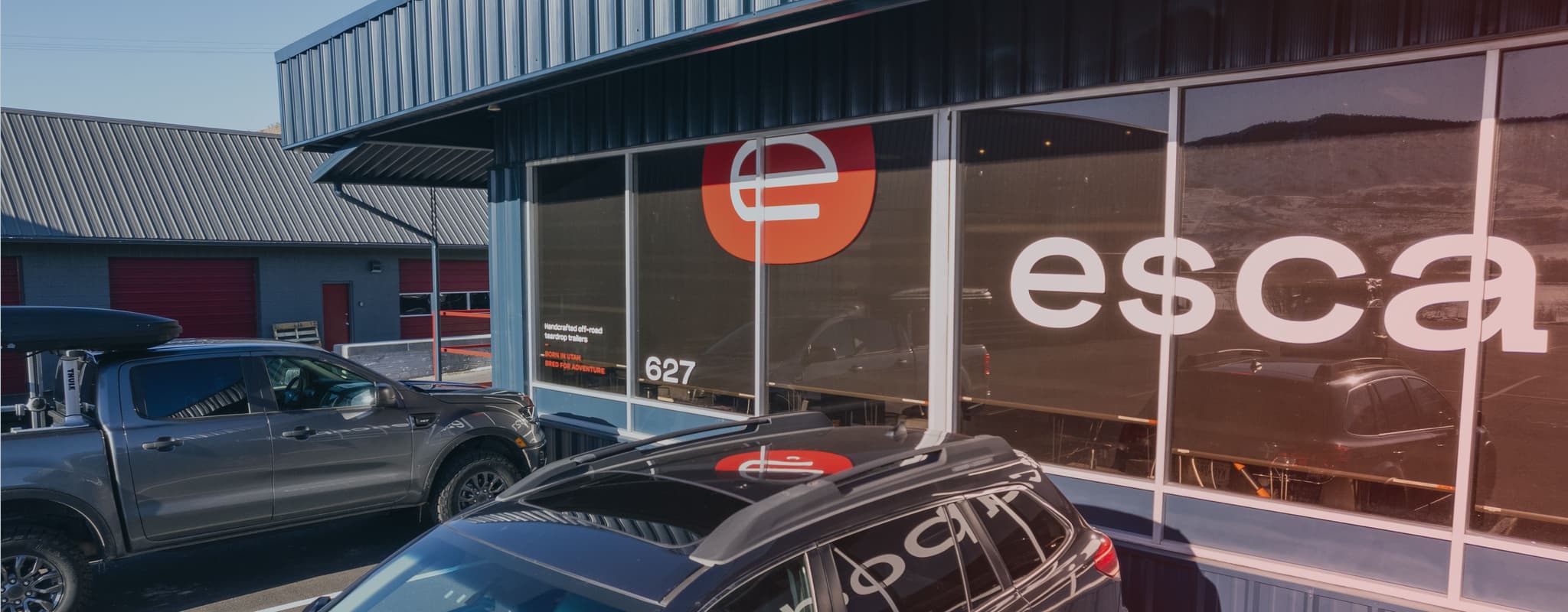 Escapod’s headquarters with the brand logo on front-facing windows, red industrial design, and adventure-ready vehicles parked outside.