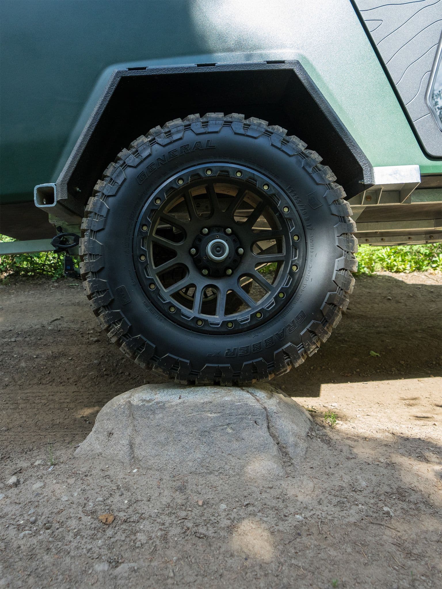 A TOPO2 rolling over a rock on an off-road trail. The green trailer has a rugged fender, Grabber X3 off road tires, and off-road Vision alloy wheels.