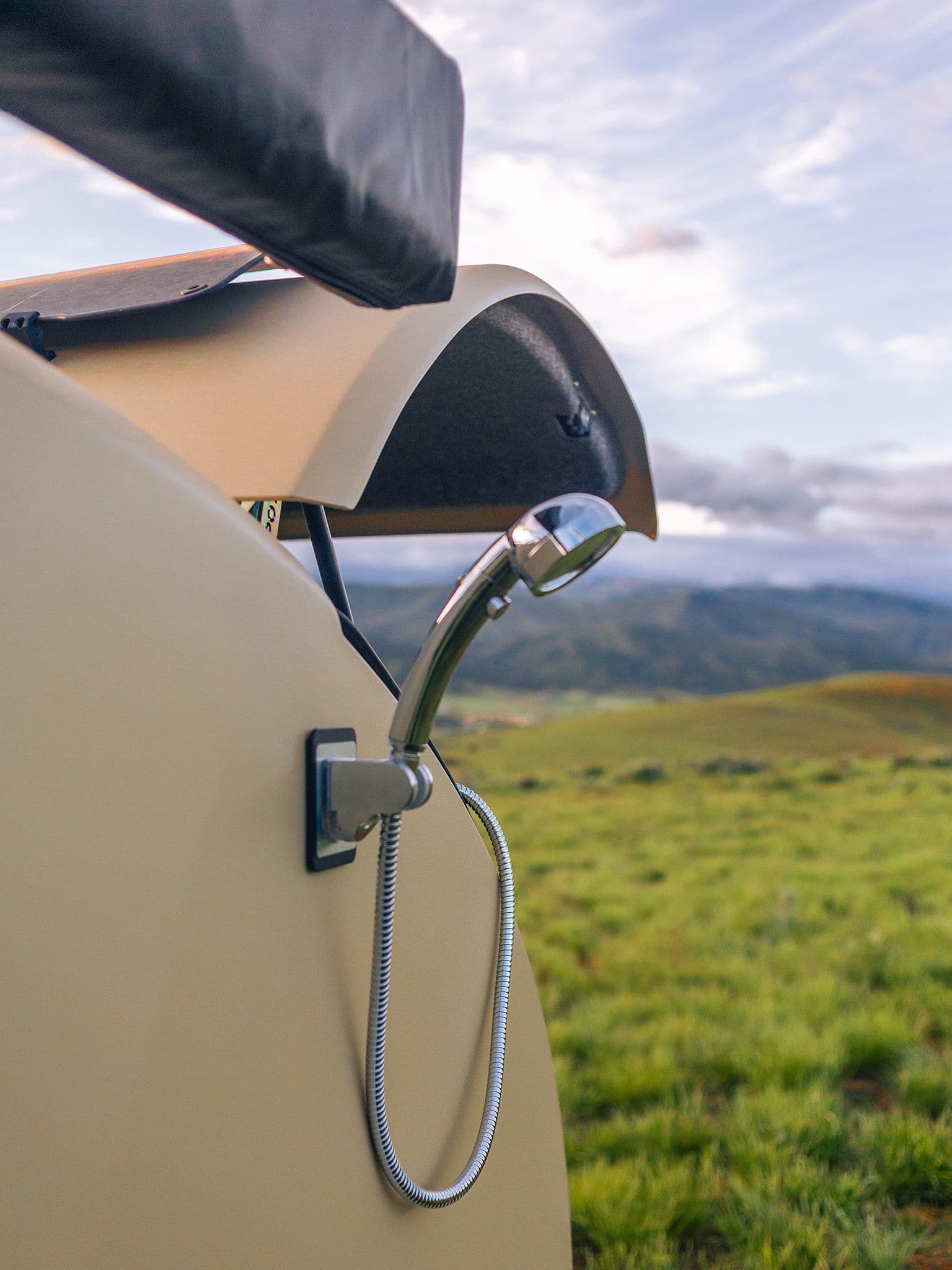 Close up of the Escapod TOPO2 with the shower handle mounted to the magnetic catch built into the body of the trailer, and the hatch open with a gassy field behind the trailer.