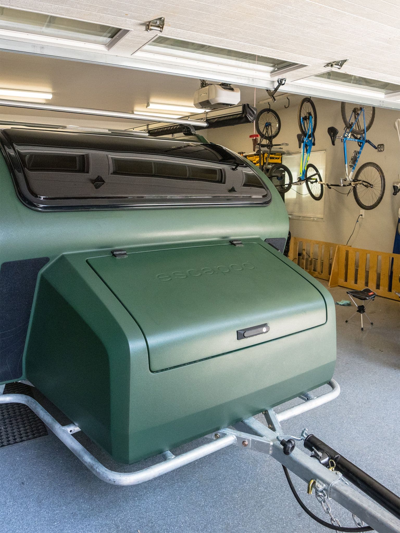 Green Escapod trailer parked in a garage alongside motorcycles and outdoor gear.