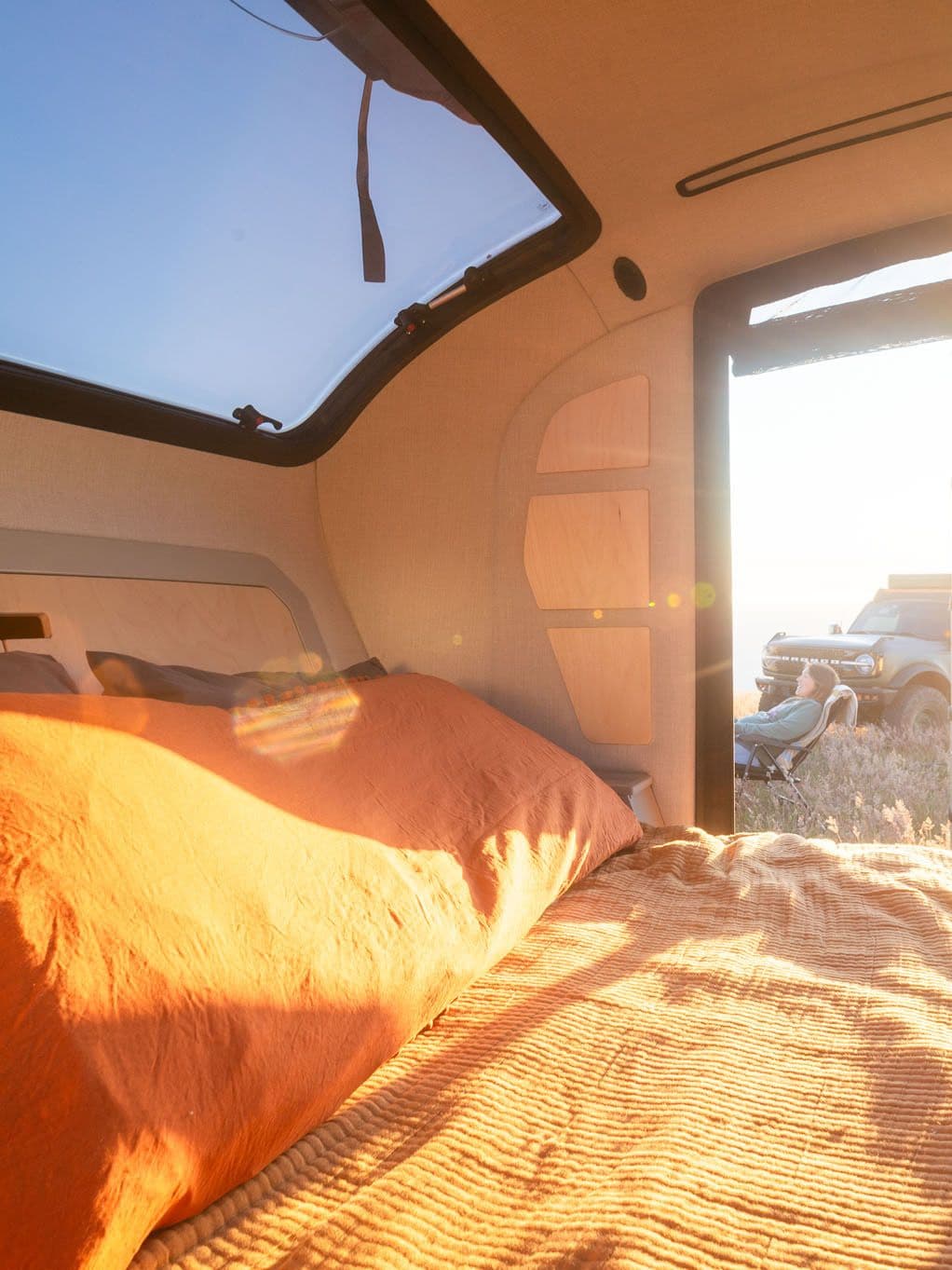 Cozy interior of an Escapod TOPO2 trailer with sunlight streaming in, showing the bed and an open door.