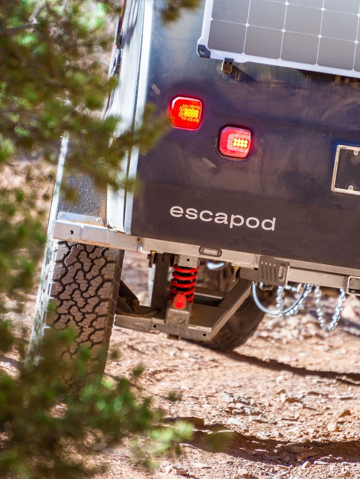 Close-up of Escapod trailer's off-road suspension system with red coil springs, rugged tires, and solar panel, built for extreme terrain.