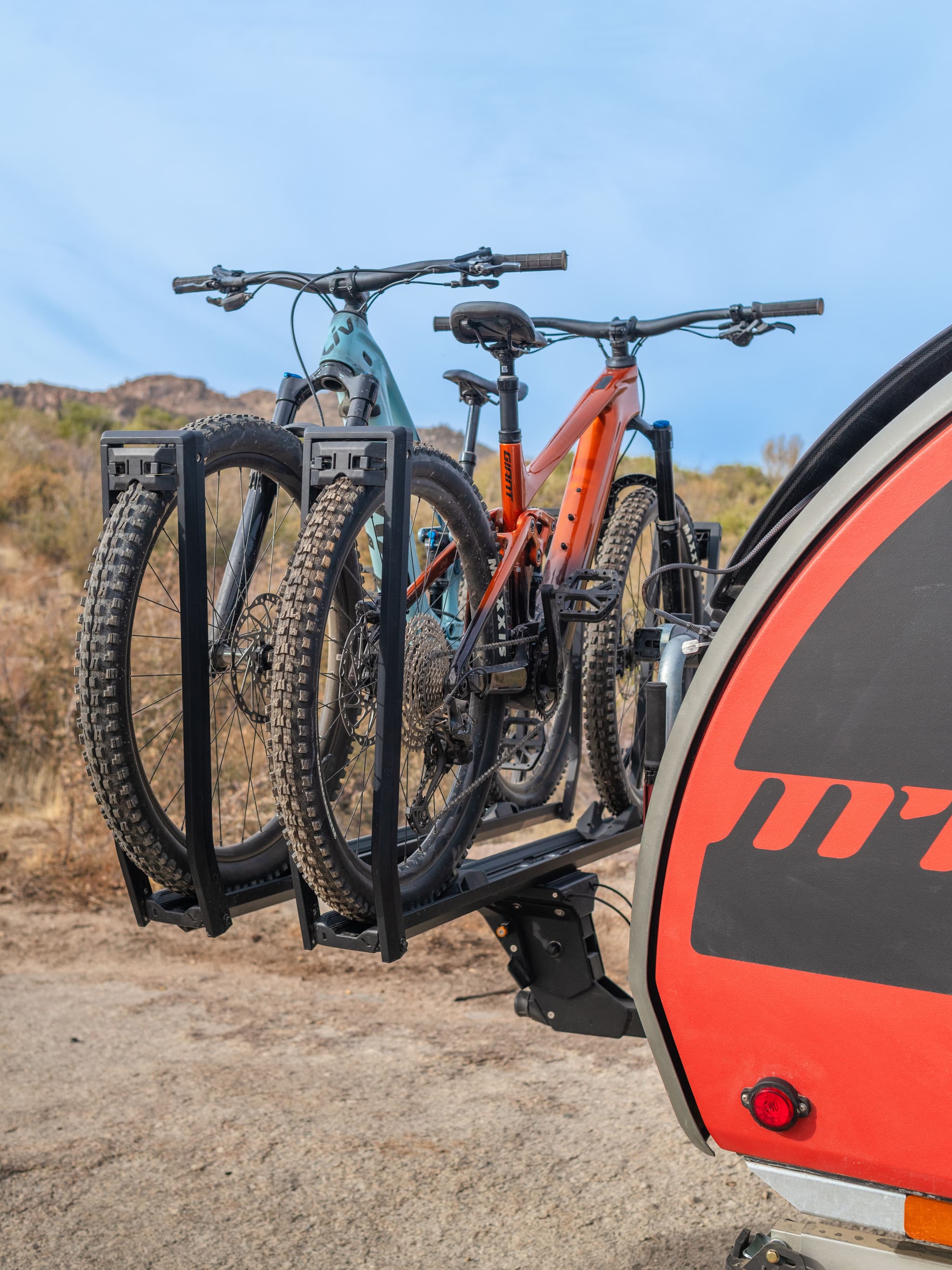 Rear angle of the TOPO2 MTB with two mountain bikes secured to the Kuat rack, showcasing the tire treads and rack design.