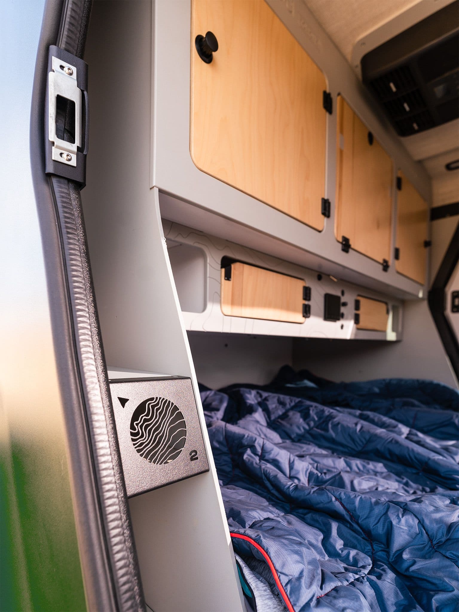 The interior of the Escapod TOPO2 photographed from the door, showing the hot air vent, and ample storage, along with a blue Rumpl blanket and a Dometic RTX1000 A/C unit.